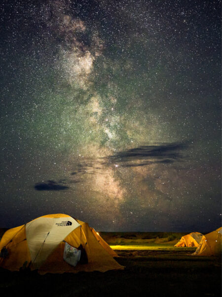 Ein Zeltcamp bei einer Trekkingreise durch die Mongolei bei Nacht. Über dem Camp sieht man den Sternenhimmel inklusive den Nebeln der Milchstraße.