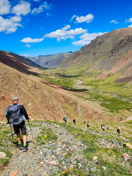 Eine kleine Gruppe auf Wanderreise geht einen Weg in ein Tal in den bergigen Landschaften der Westmongolei hinab.