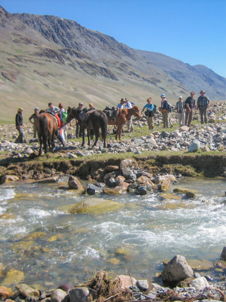 Eine Gruppe auf Wanderreise durch die Mongolei steht mit ihren Packtieren vor einem Gewässer im Vordergrund.