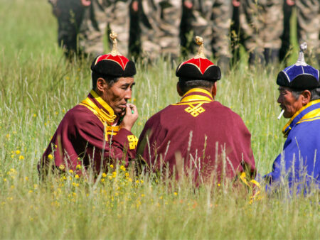 Drei Männer in traditioneller mongolischer Kluft sitzen gemeinsam in der Wiese.