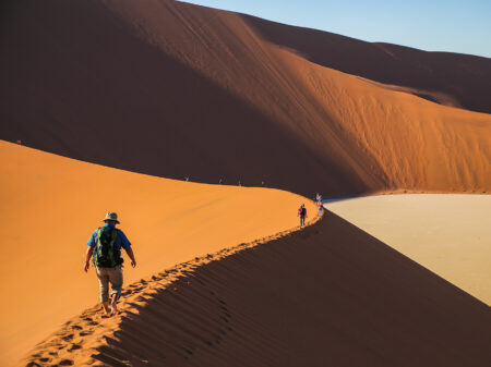 Reisende wandern über hohe Sanddünen im Sossusvlei in der Namib-Wüste.