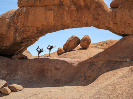 Zwei Personen machen Yoga unter einem Felsbogen im Erongo-Gebirge in Namibia.
