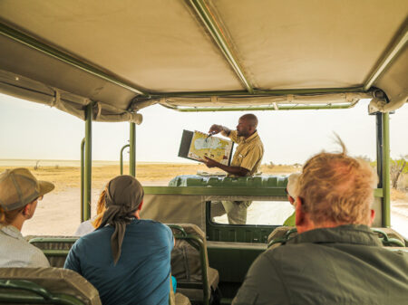 Safari-Guide erklärt Gästen die Route während einer Jeepsafari in der Savanne Namibias.