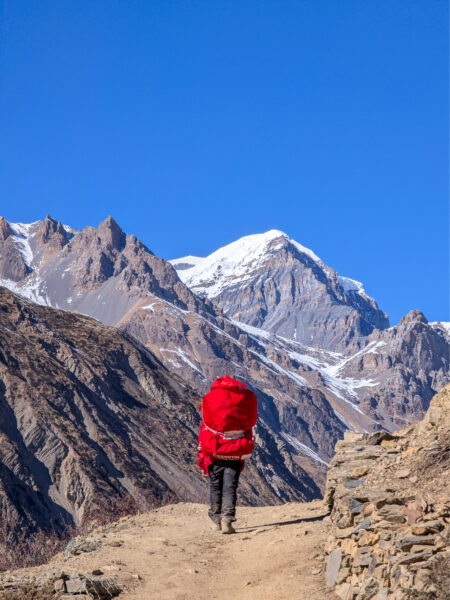 Ein Wanderer mit einem großen, roten Rucksack der Reiseanbieters Weltweitwandern folgt einem Trekking-Pfad in der Nähe des Annapurna-Massivs.