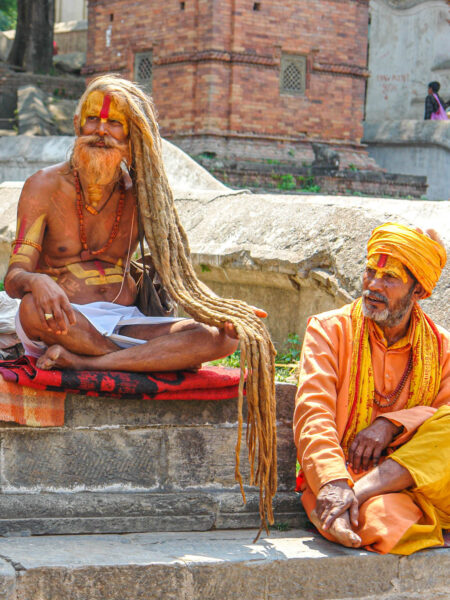 Zwei nepalesische Männer sitzen auf Stufen. Beide tragen traditioneller Gewänder, einer hat ausgesprochen langes Haar, der andere trägt einen Turban.