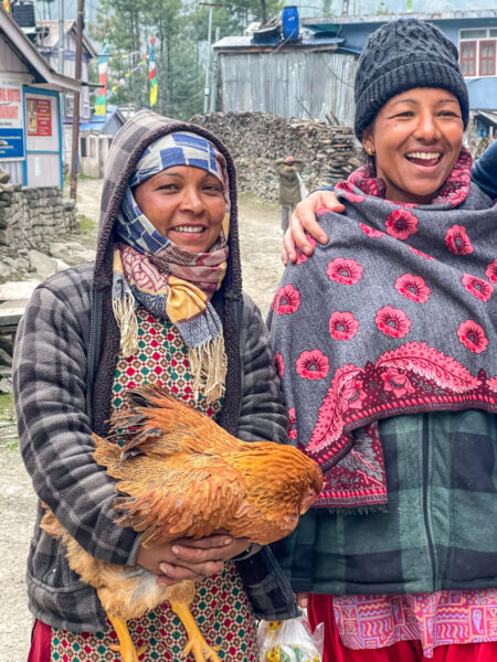 Zwei nepalesische Frauen Lächeln in die Richtung der Kamera. Eine von ihnen hält ein Huhn.