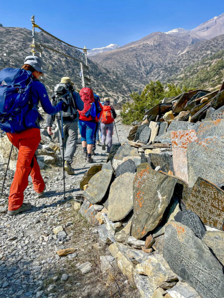 Mehrere Personen mit Wanderausrüstung folgen einem Weg entlang des Annapurna-Circuit. Die Gehen ihrem lokalen Guide hinterher, der sie durch den Himalaya führt.