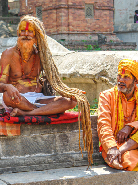 Zwei Sadhus, hinduistische Asketen, aus einem Tempel in Kathmandu, sitzen auf den Stufen und folgen mit dem Blick etwas, das nicht im Bild zu erkennen ist.