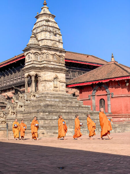 Eine Gruppe junger Mönche folgt einem älteren Mönch über den Durbar Square in Bhaktapur. Hinter ihnen sieht man den Siddhi Lakshmi Tempel.