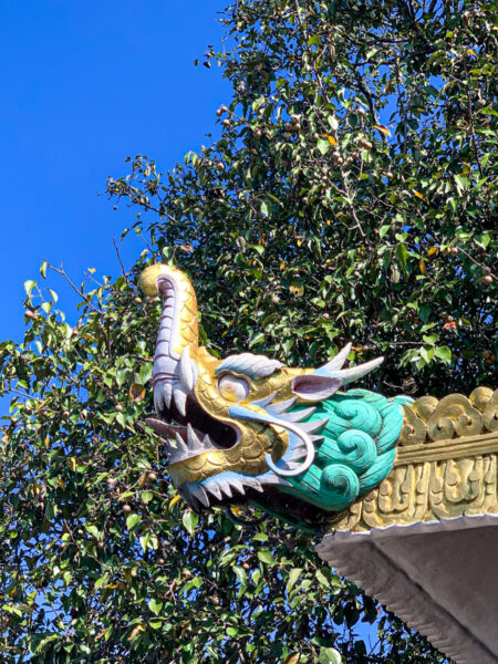 Man sieht eine Verzierung eines Daches oder einer Pagode in dem buddhistischen Kloster Namobuddha in Nepal. Die Verzierung sieht aus wie ein Hybrid aus einem Drachen und eine Elefanten.