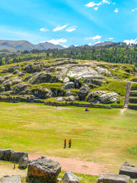 Zwei Personen stehen in der Wiese in einem Teil der alten Befestigungsanlage Sacsayhuamán in der Nähe von Cusco in Peru. Die beiden Personen auf Wanderreise sind umgeben von der historischen Stätte.