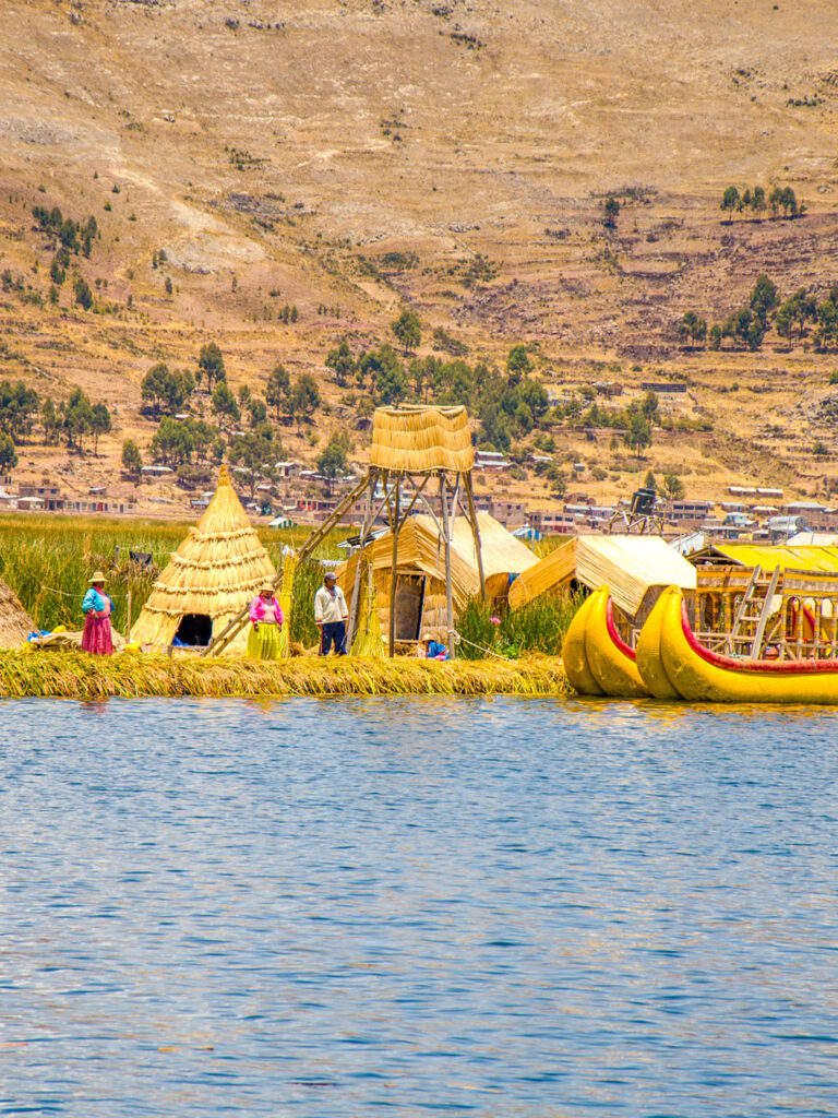 Man sieht die schwimmenden Inseln der Uros in Peru sowie mehrere ihrer bemalten Boote über das Wasser hinweg. Hier übernachten auch Gäste auf einer Weltweitwandern-Reise durch Peru.