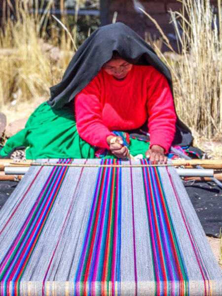 Eine Einheimische auf der Insel Taquile im Titicaca-See webt auf traditionelle Art und Weise einen bunten Stoff.
