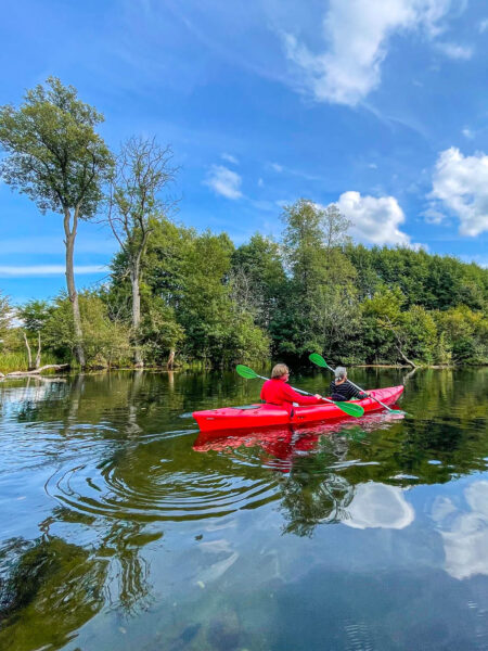 Zwei Wanderreisende sitzen gemeinsam in einem Kanu auf dem Fluss Krutynia in Polen. Sie sind Teil einer geführten Kanugruppe auf ihrer Reise durch die Masuren in Richtung Ostsee.