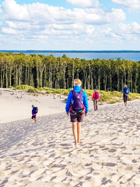 Eine Frau steh in in den Dünen der Ostsee, sie trägt einen Rucksack für ihre Wanderreise, die sie durch die Masuren bis zur Küste bringt.