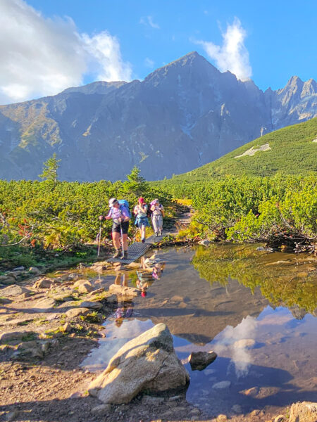 Mehrere Personen auf Wanderreise gehen am Ufer des Strbské Pleso, des dreieckigen Sees, einem Bergesse in der Tatra entlang.