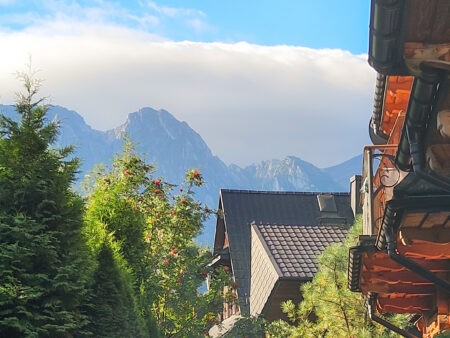 Ein Ausblick auf die Tatra von einer Unterkunft in Zakopane aus. Wolken hängen hinter dem Gebirgszug, der das Grenzland zwischen Polen und der Slowakei bestimmt, im Vordergrund ragen Baumwipfel ins Bild.