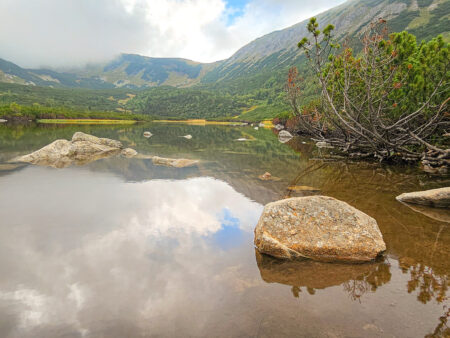 Man sieht den Weißen See, einen Bergsee in der Hohen Tatra, wo Wanderreisende mit Weltweitwandern zu einer kleinen Pause eingeladen werden Im Hintergrund sieht man die wolkenverhangenen Berg der Tatra.