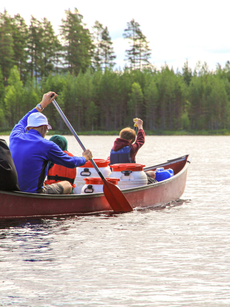 Zwei Personen rudern in einem kleinen Boot über einen See in Schweden. Im Hintergrund sieht man Nadelwälder, die man auch auf der geführten Reise mit Weltweitwandern erkunden kann.