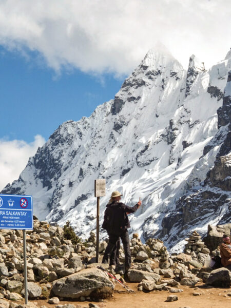 Zwei Wanderinnen steht auf einem Felsvorsprung in den Anden und machen ein Selfie. Im Hintergrund kann man einen schneebedeckten Berghang erkennen.