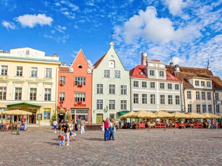 Mehrere Personen auf Wanderreise in der Region gehen gerade über den Rathausplatz in Talinn, der mit arbenprächtigen Gebäuden besticht.