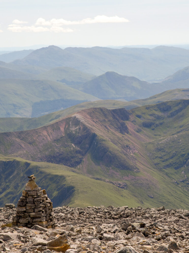 Man sieht die Aussicht nach dem Aufstieg auf den Ben Nevis, den höchsten Berg auf den britischen Inseln. Im Vordergrund sieht man einen der vielen Cairns, Steinpyramiden, die den Weg bis zum Gipfel des Berges begleiten.