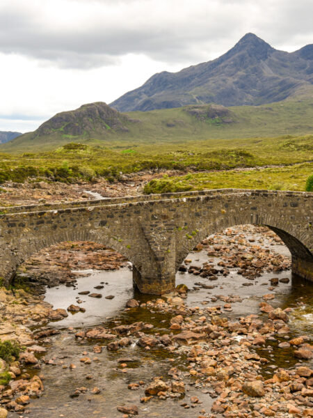 Die Sligachan Old Bridge spannt sich im Bild über einen Fluss auf der Isle of Skye in Schottland.