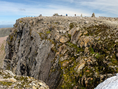 Ein Panoramafoto des Ben Nevis aus einiger Distanz. Auf dem Gipfel des höchsten Berges Schottlands kann man mehrere Personen auf Wanderreise sowie auch zwei Cairns erkennen.