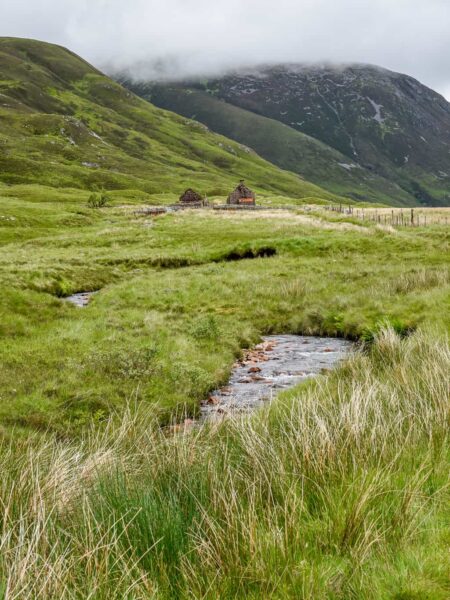 Man sieht die schottischen Highlands, inklusive eines kleinen Gewässers, das zwischen den grünen Wiesen sichtbar ist.