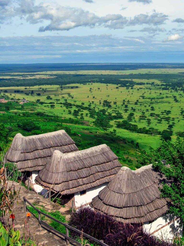 Das Landschaftsfoto zeigt den Queen Elizabeth Nationalpark in Uganda im Hintergrund und mehrere strohgedeckte Gebäude der Kingfisher Lodge im Vordergrund des Bildes.