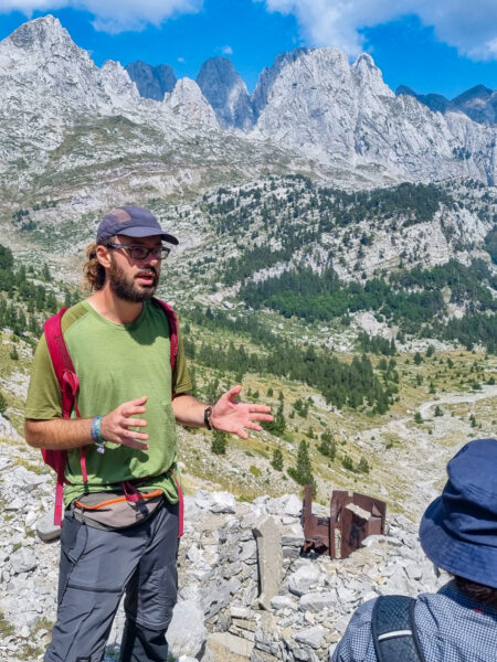 Ein Guide von Weltweitwandern erklärt seiner Gruppe etwas über die Bunker, die vielerorts in Albanien errichtet wurden. Hinter ihm sieht man einen davon im Berg.