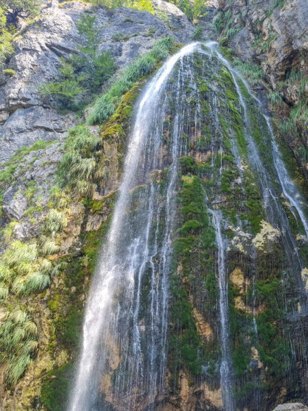 Der Wasserfall von Teth kommt in dem Foto aus dem Fels hervor und rinnt ins Tal hinab.