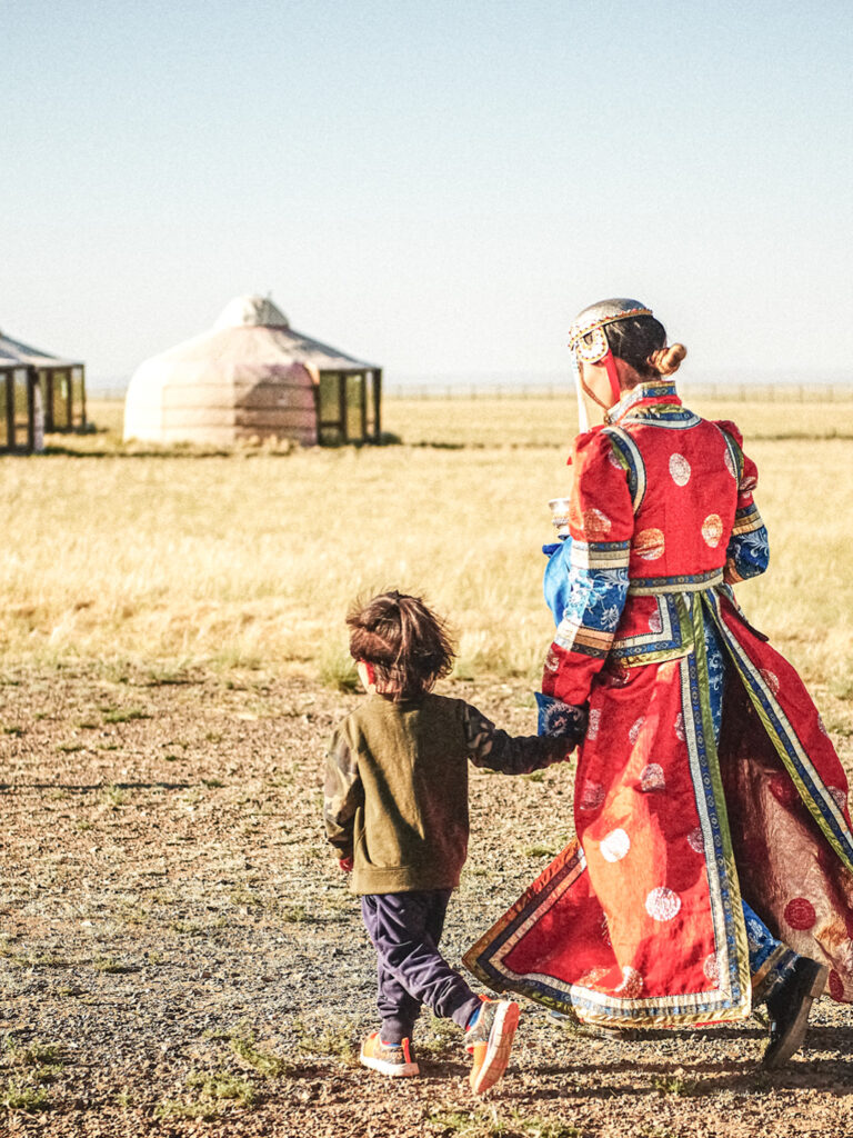 Eine Einheimische mit Kind geht durch ein Zeltlager in der Monolei. Man sieht im Hintergrund mehrere Jurten.