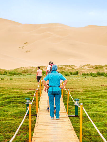 Eine Wanderreisende steht auf einem Steg in der Mongolei. Im Hintergrund kann man die Wüste Gobi erkennen.