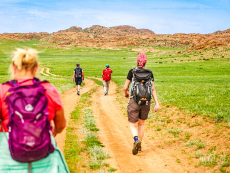 Vier Personen auf Wanderreise gehen auf einem Weg durch eine Ger in der Mongolei.