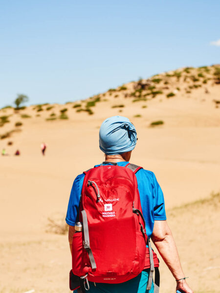 Eine Frau mit einem roten Rucksack von Weltweitwandern geht durch die Wüste Gobi in der Mongolei.