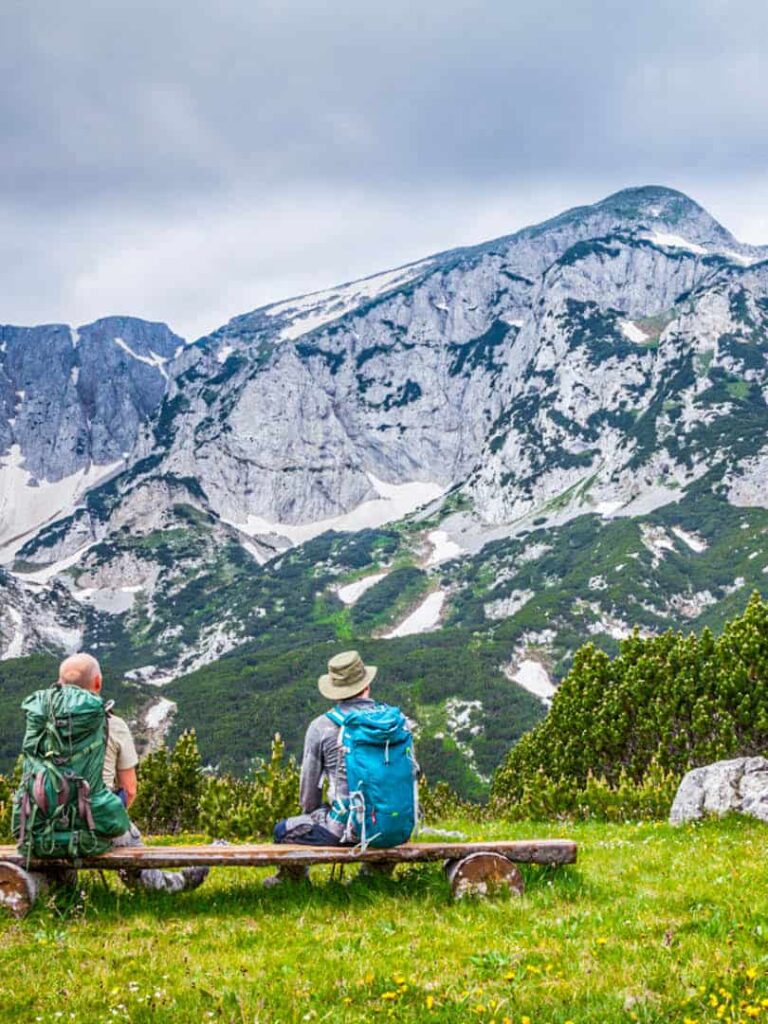 Zwei Wanderer sitzen auf einer Bank inmitten der Bergewelt Bosniens und schauen hinaus auf das Panorama, das sich ihnen hier auf ihrem Wanderurlaub bietet.