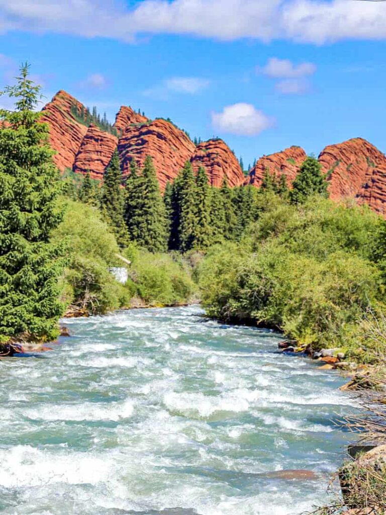 Auf dem Bild sieht man mehrere der Jety-Ögüz, einer bekannte Felsformation in Kirgistan. Im Vordergrund fließt ein Fluss, den man auch im Zuge einer Wanderreise begeht.