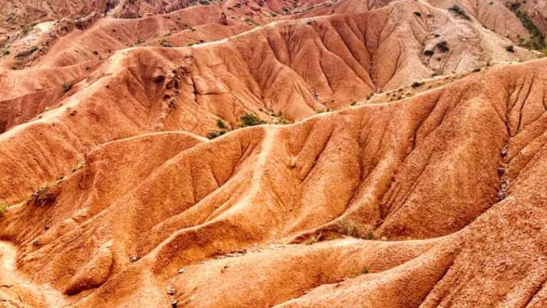 Ein Wanderer geht durch die Märchenschlucht in Kirgistan, die bekannt ist durch ihre rote Erde und außergewöhnlichen Felskonstellationen.