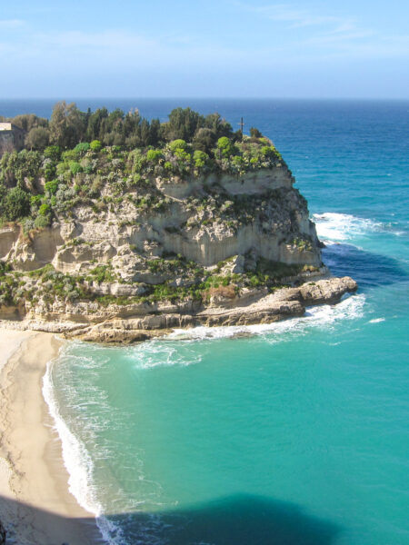 Man sieht ein der italienischen Küste am tyrrhenischen Meer. Im Vordergrund ist Sandstrand sichtbar, während dahinter steile Klippen hinter dem Santuario di Santa Maria dell'Isola aufragen. Das Kloster nach Tropea ist auf dem Bild nicht zu sehen.