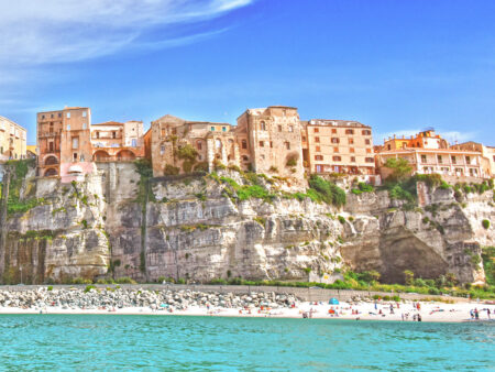 Die Gebäude von Tropea ragen über den Strand am tyrrhenischen Meer hinaus. Die rötlichen Gebäude der italienischen Ortschaft stehen dabei bis an den Rand von imposanten Klippen.