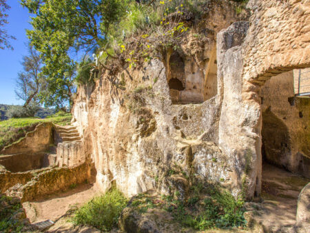 Ein steinerner Eingang der mittlalterlichen Höhlenstadt Zungri auf der Halbinsel Kalabrien in Italien ist am Bild zu erkennen. Die Ruinen stehen im harten Kontrast zu dem strahlend blauen Himmel Italiens im Hintergrund.