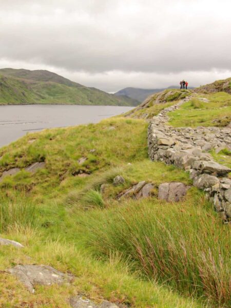 Man sieht den Killary Harbour in Irland von einem Wanderweg aus. Außerdem ist im Bild eine niedrige Steinmauer zu erkennen, die Irlands Landschaft vierlerorts prägt.