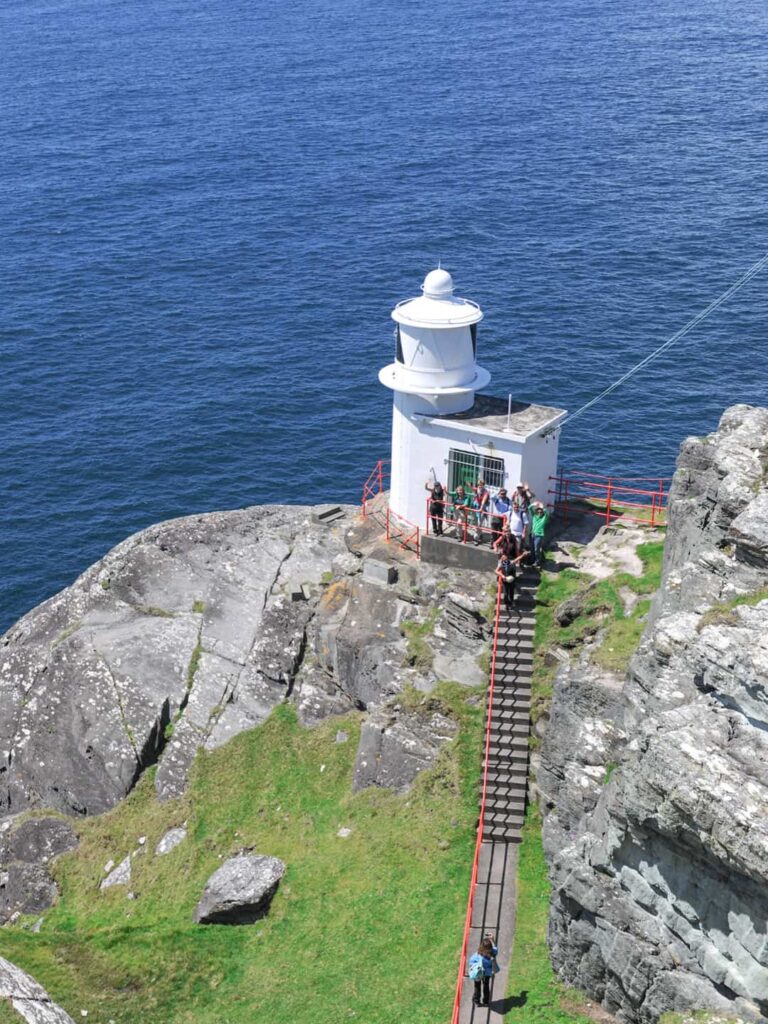 Eine kleine Gruppe auf einer Wanderreise steht vor dem Sheep's Head Lighthouse auf der gleichnamigen Insel vor der Küste Irlands.