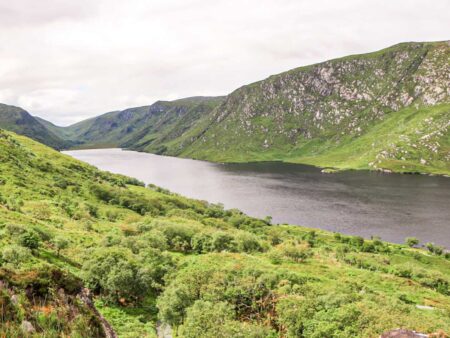 Man sieht den See Lough Veagh im Glenveagh Nationalpark in Irland. Der See liegt zwischen grüne Wiesen eingebettet in der Landschaft.
