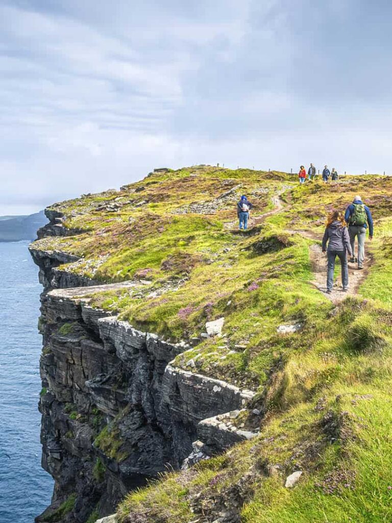 Mehrere Personen auf einer Wandererise mit Weltweitwandern folgen einem Pfad entlang der Cliffs Moher in Irland.