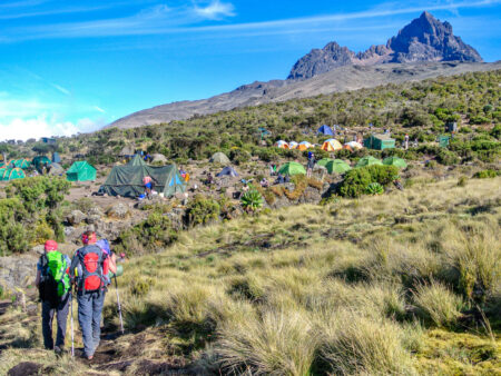 Zwei Wander*innen gehen auf ein Zeltlager am Weg zum Gipfel des Kilimandscharo zu.