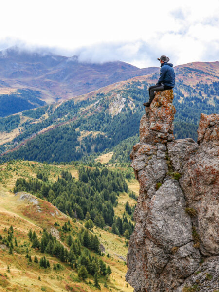 Ein Guide von Weltweitwandern sitzt auf Felsvorsprung und schaut hinaus auf einen der Nationalparks im Balkan. Die Landschaft des gebirgigegen Grenzlandes zwischen Albanien, Montenegro und Kosovo breitet sich hinter und unter ihm im Tal aus.