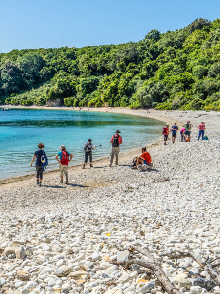 Mehrere Personen auf einer Wanderreise gehen über den Strand von Akoli an der Nordküsten von Korfu.