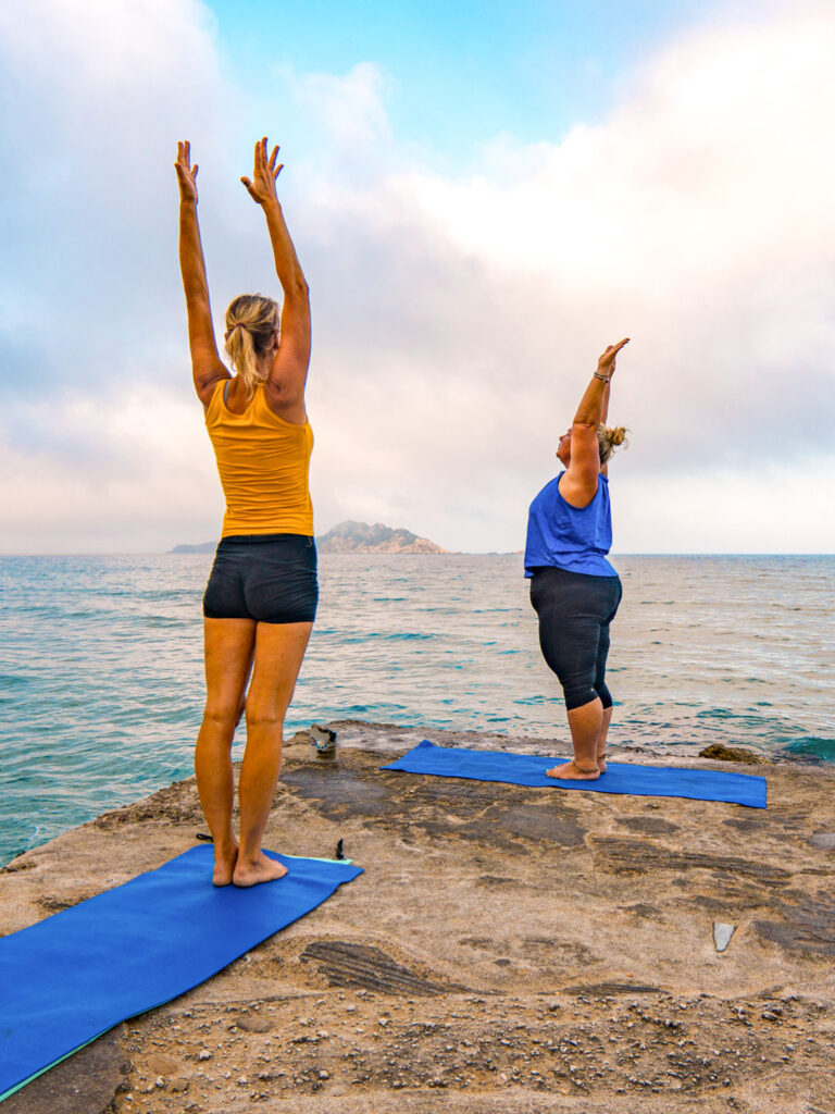Zwei Frauen auf Wanderreise in Griechenland machen an der Küste von Korfu Yoga. Sie werden angeleitet durch eine der Guide von Weltweitwandern auf der Insel.